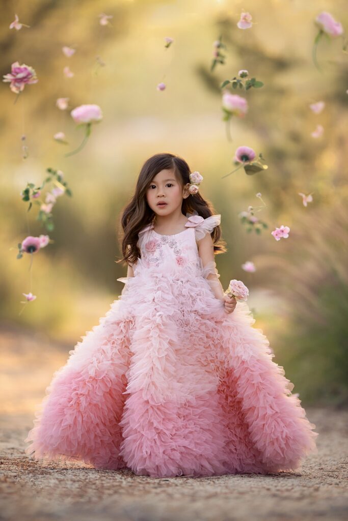 A young girl stands among falling flowers in a large pink dress at sunset while attending the Best private schools in Orange County