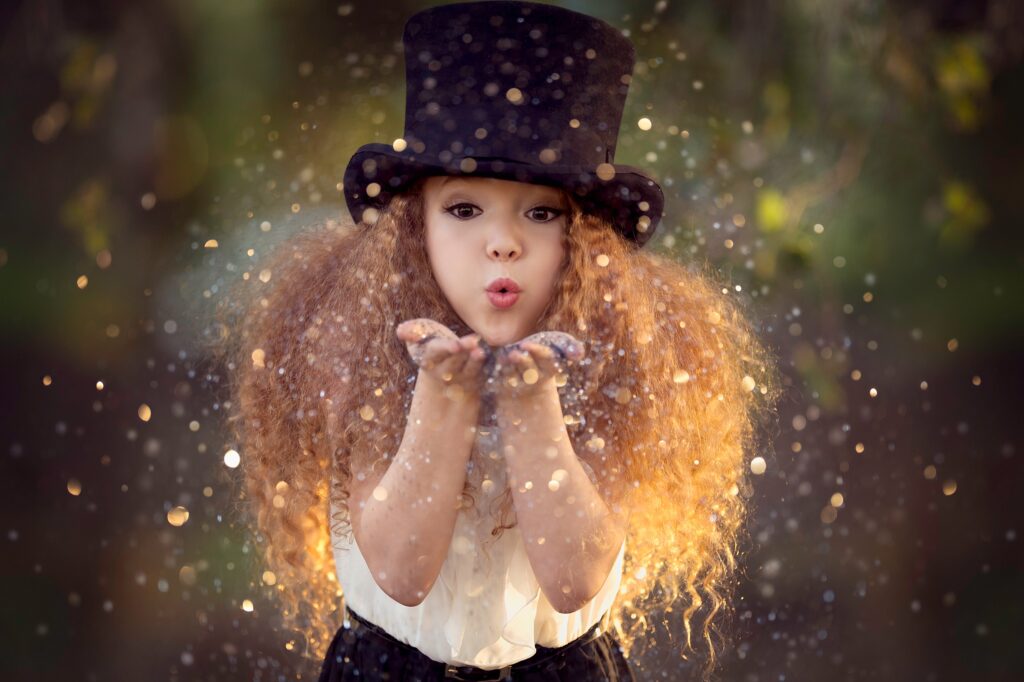 A young girl in a large tophat blows glitter in front of her