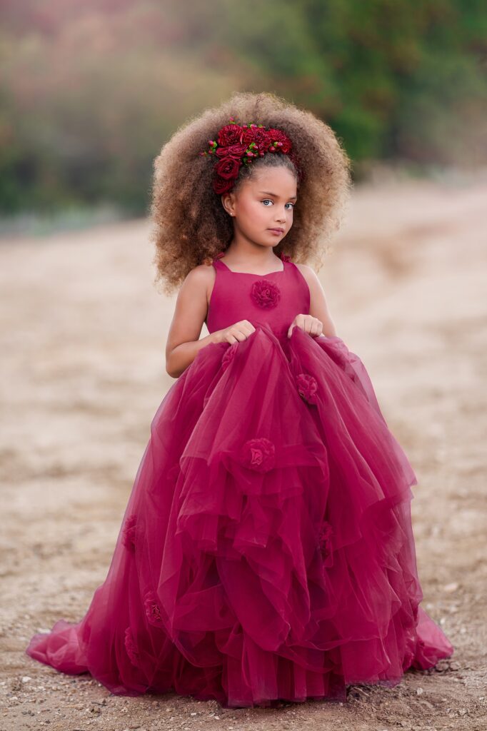 A young girl in a large red dress walks through a park path after visiting orange county baby boutiques
